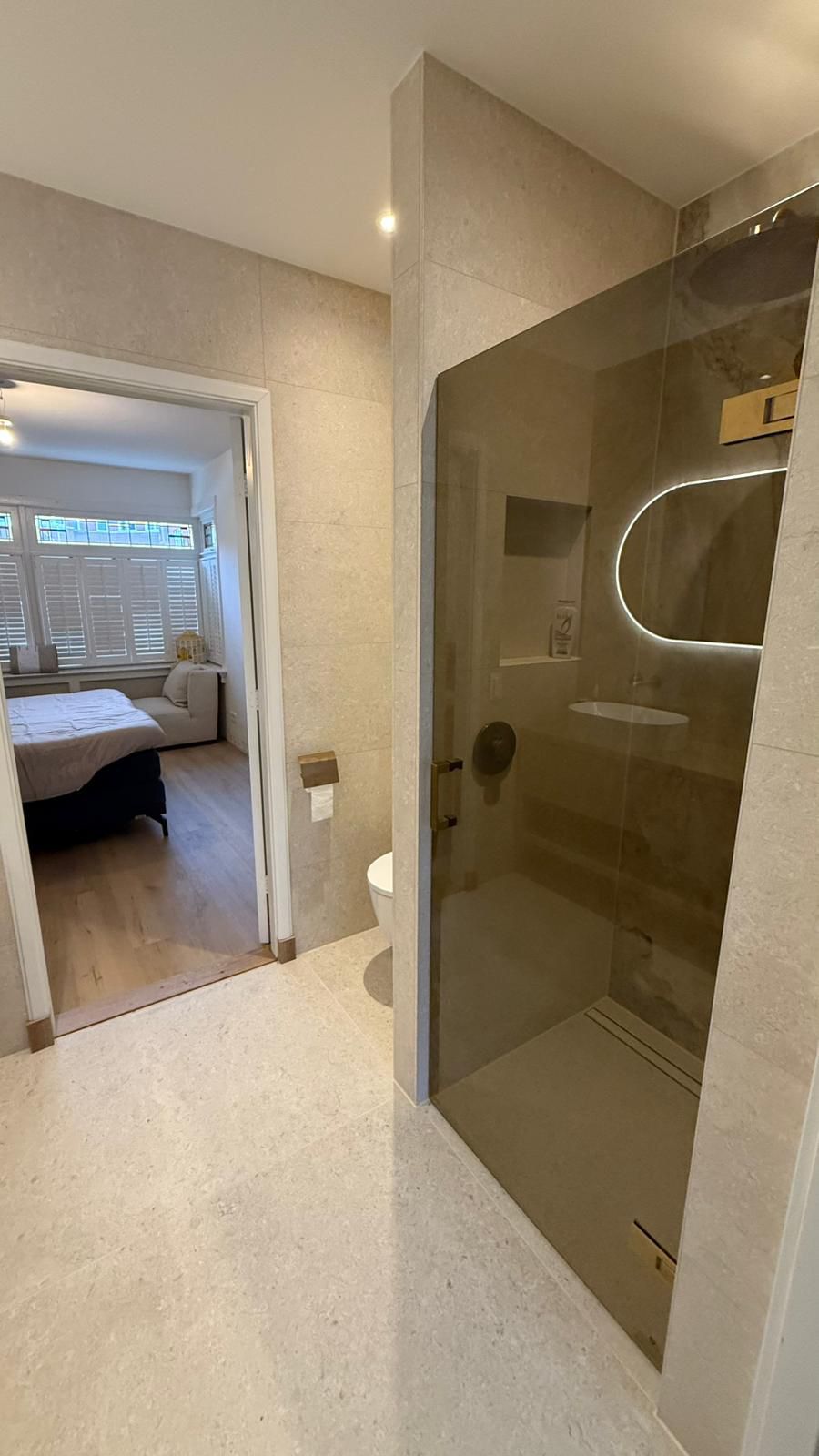 Badkamer met crème marmerlook tegels, rookglas douchewand en bronzen accenten