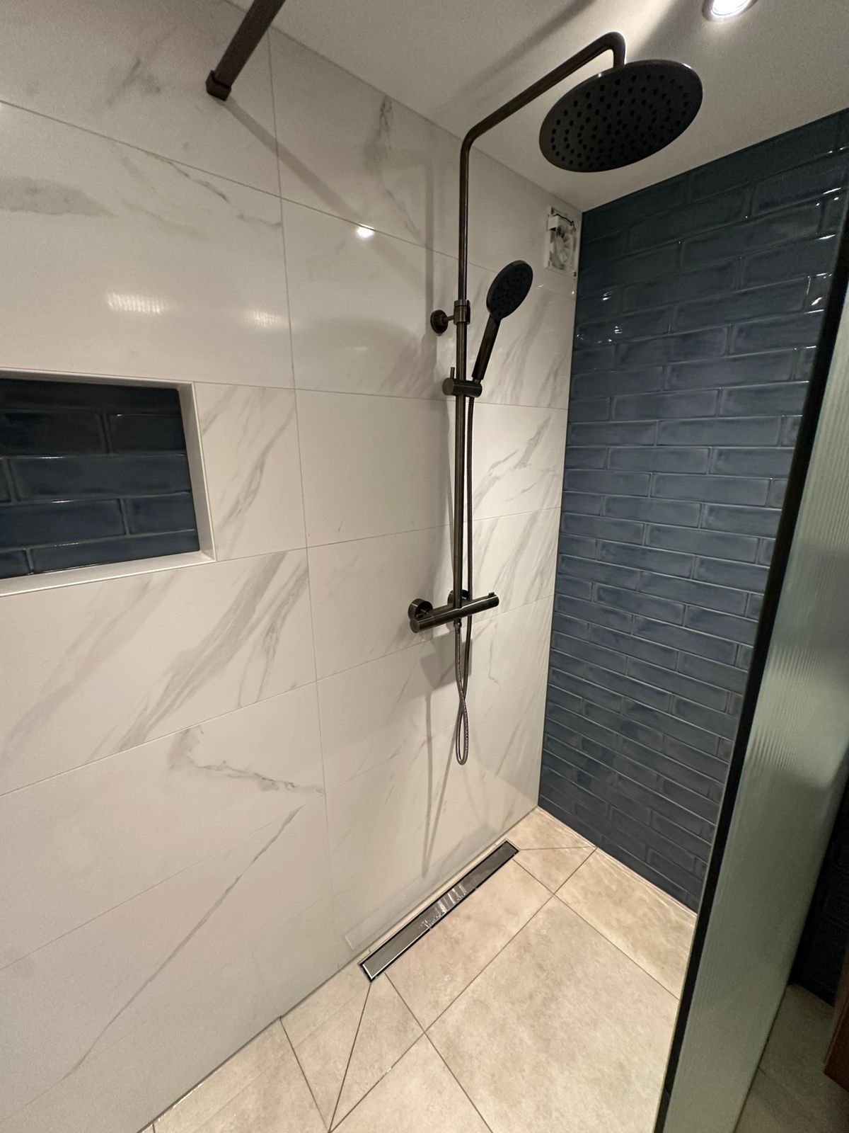 Vernieuwde inloopdouche met wit marmer en marineblauw tegelaccent